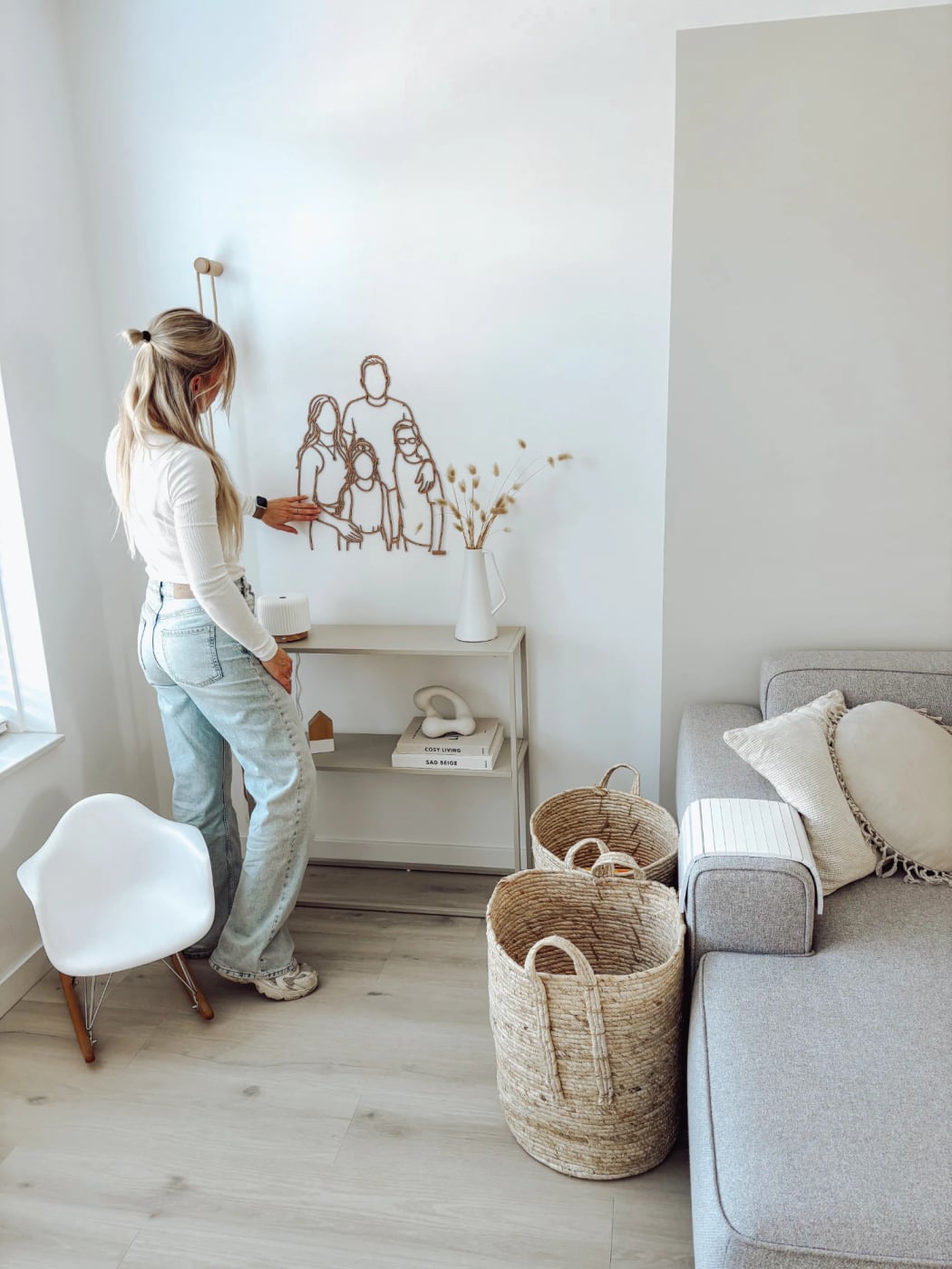 Houten gezinsportret aan de muur boven een open kast, in een rustige, lichte woonkamer